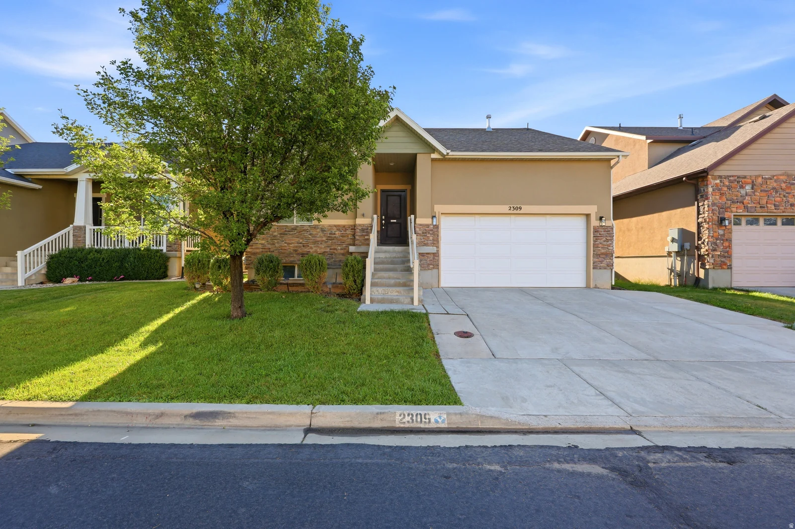 Stucco and stone facade with a prominent two-car garage, concrete driveway, and front lawn
